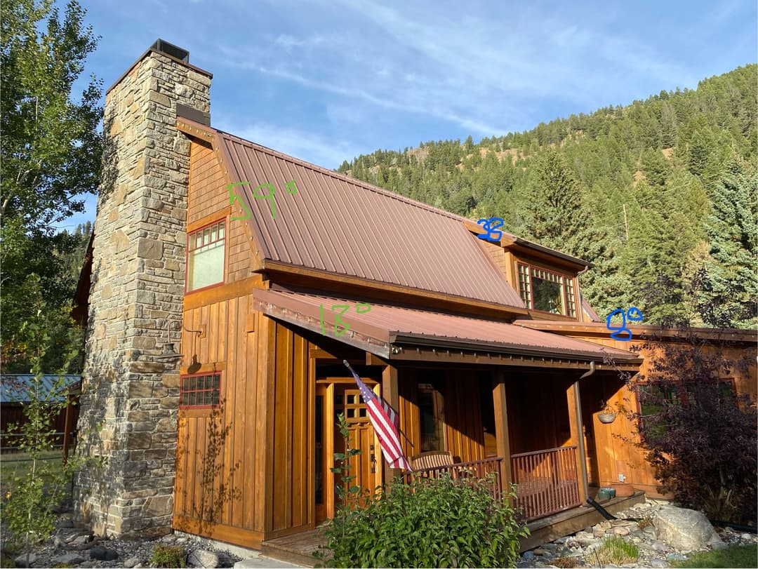 Charming wooden cabin with stone chimney, sloped roofs, and lush mountain backdrop.